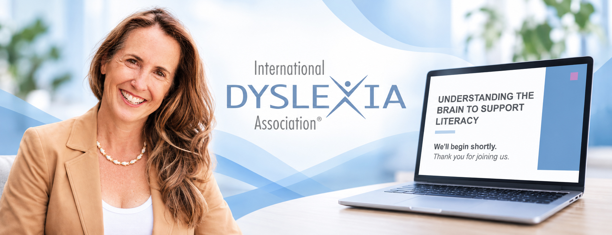 Smiling woman in a tan blazer sits beside a laptop; banner behind reads International Dyslexia Association and Understanding the Brain to Support Literacy.